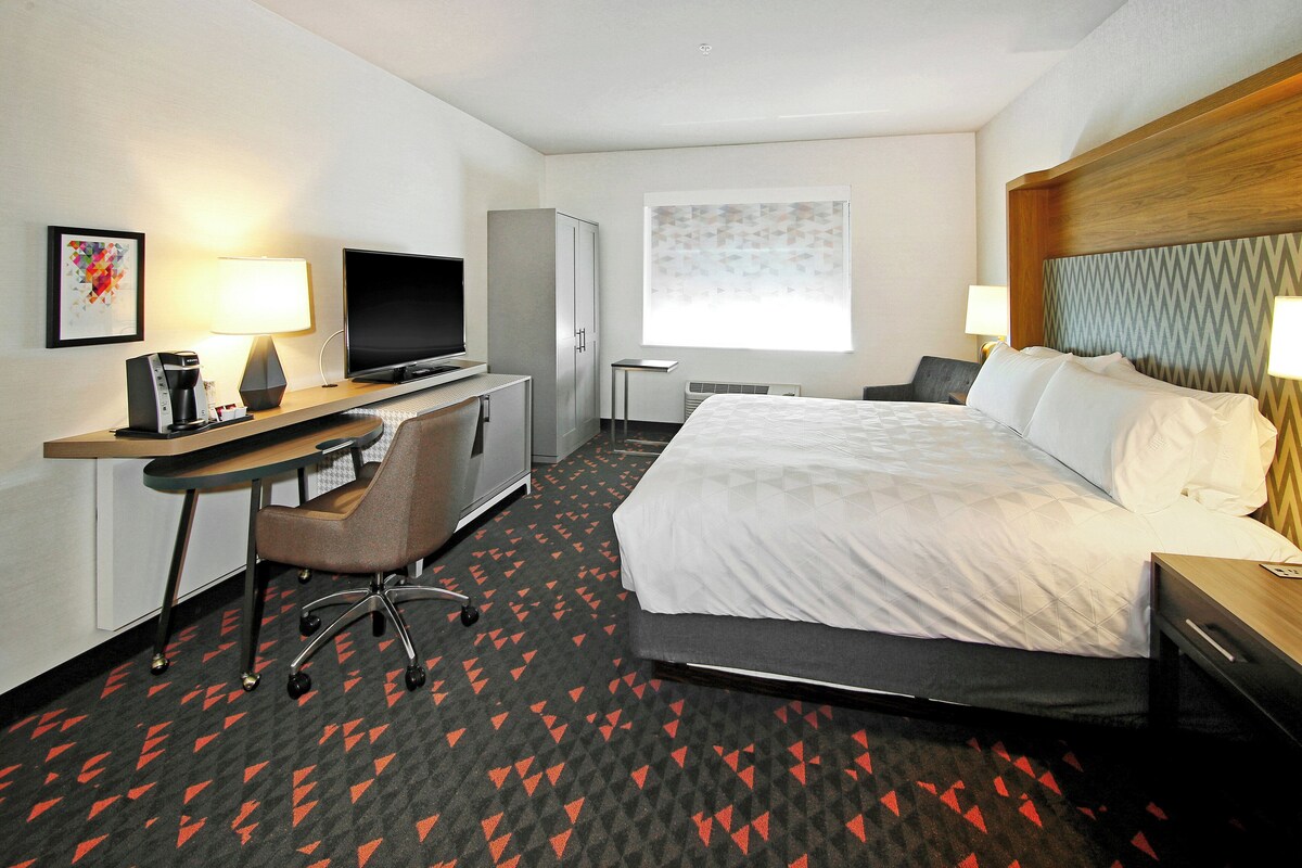A hotel room with a bed, desk, chair, television, wardrobe, and a window with a view.