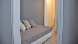 A small, narrow room with a bed against the left wall, a door to the right, and a light-colored floor. - Dimora 16 Rooms & Garden (Prato)