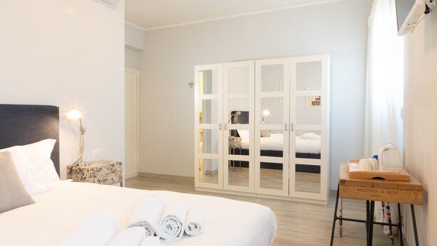 A hotel room with a bed, a nightstand, a lamp, a wardrobe, and a small table with a tray. - Dimora 16 Rooms & Garden (Prato)
