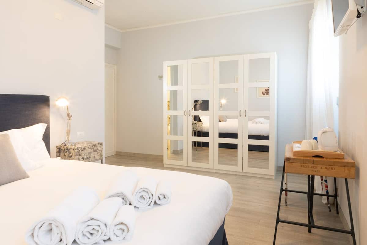 A hotel room with a bed, a nightstand, a lamp, a wardrobe, and a small table with a tray.