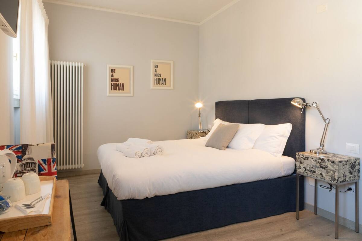 A neatly made bed with white linens and a dark headboard, a bedside table with a lamp, and two motivational posters on the wall.