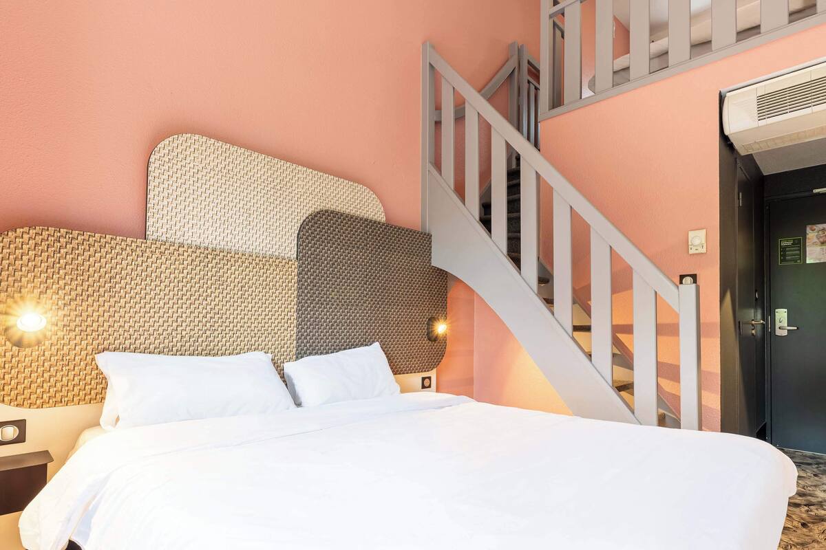 Een hotelkamer met een bed, nachtkastje, wandlamp en een trap.