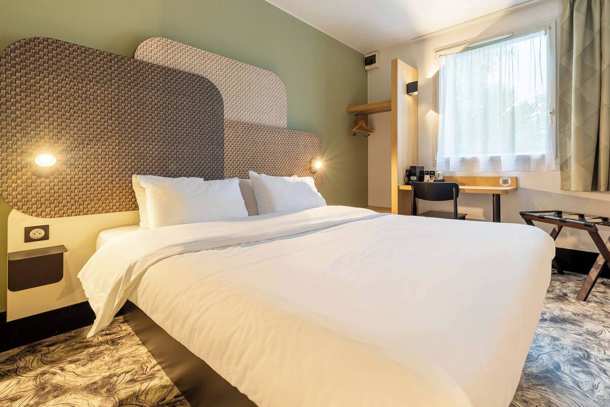 Een hotelkamer met een groot bed, een bureau, een stoel en een raam met gordijnen.