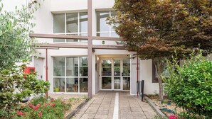 Un bâtiment moderne avec une entrée en verre, une enseigne ornée d’un logo vert et un chemin menant à l’entrée.
