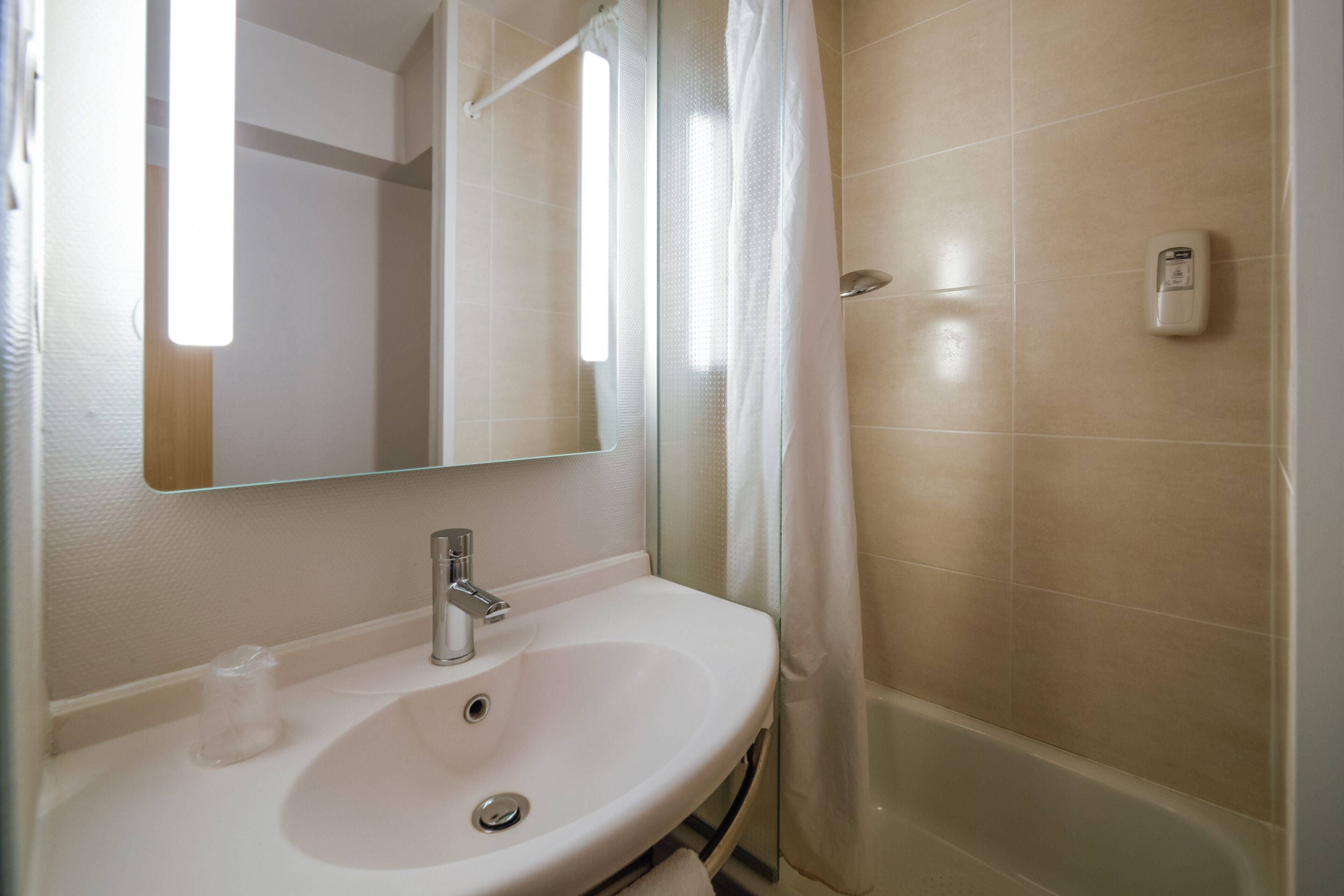 Un baño con un lavamanos blanco, un espejo, una cortina de ducha y un secador de manos.