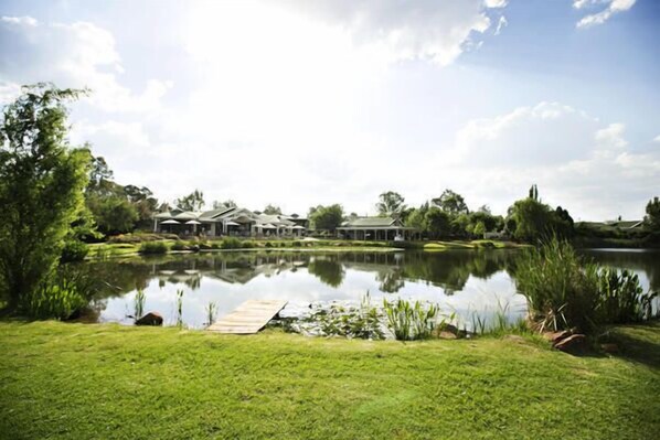 A serene lakeside property with a well-maintained lawn, a wooden dock, and a building with a covered patio area.