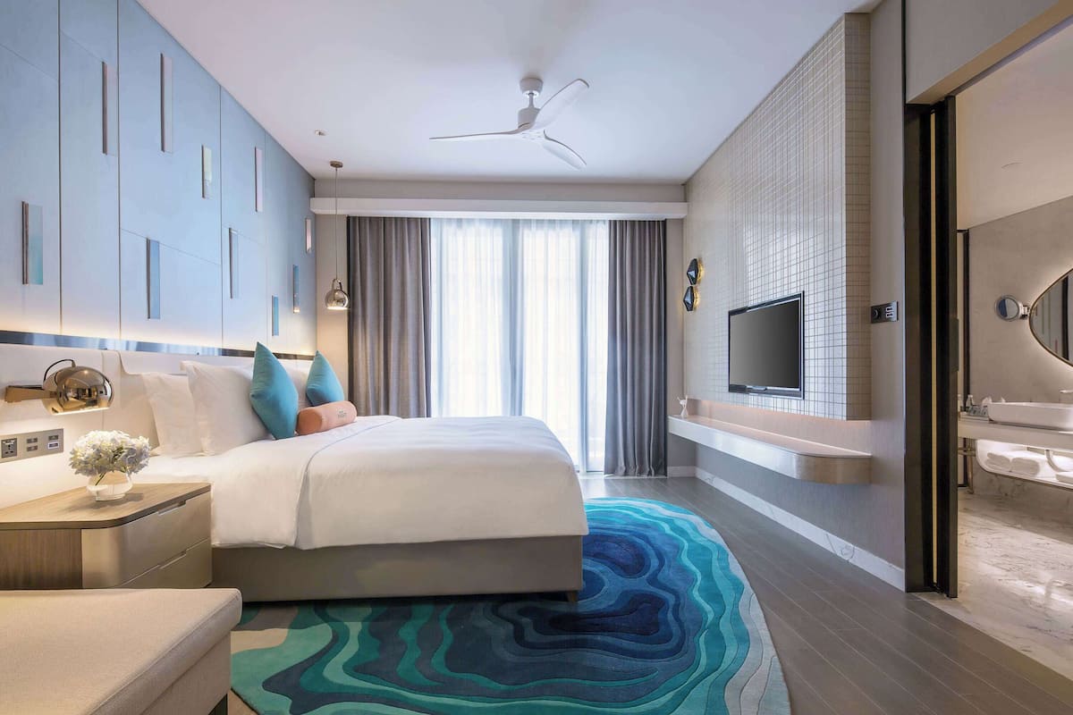 Een moderne hotelkamer met een bed, een televisie, een badkamer met een wastafel en een groot raam met gordijnen.