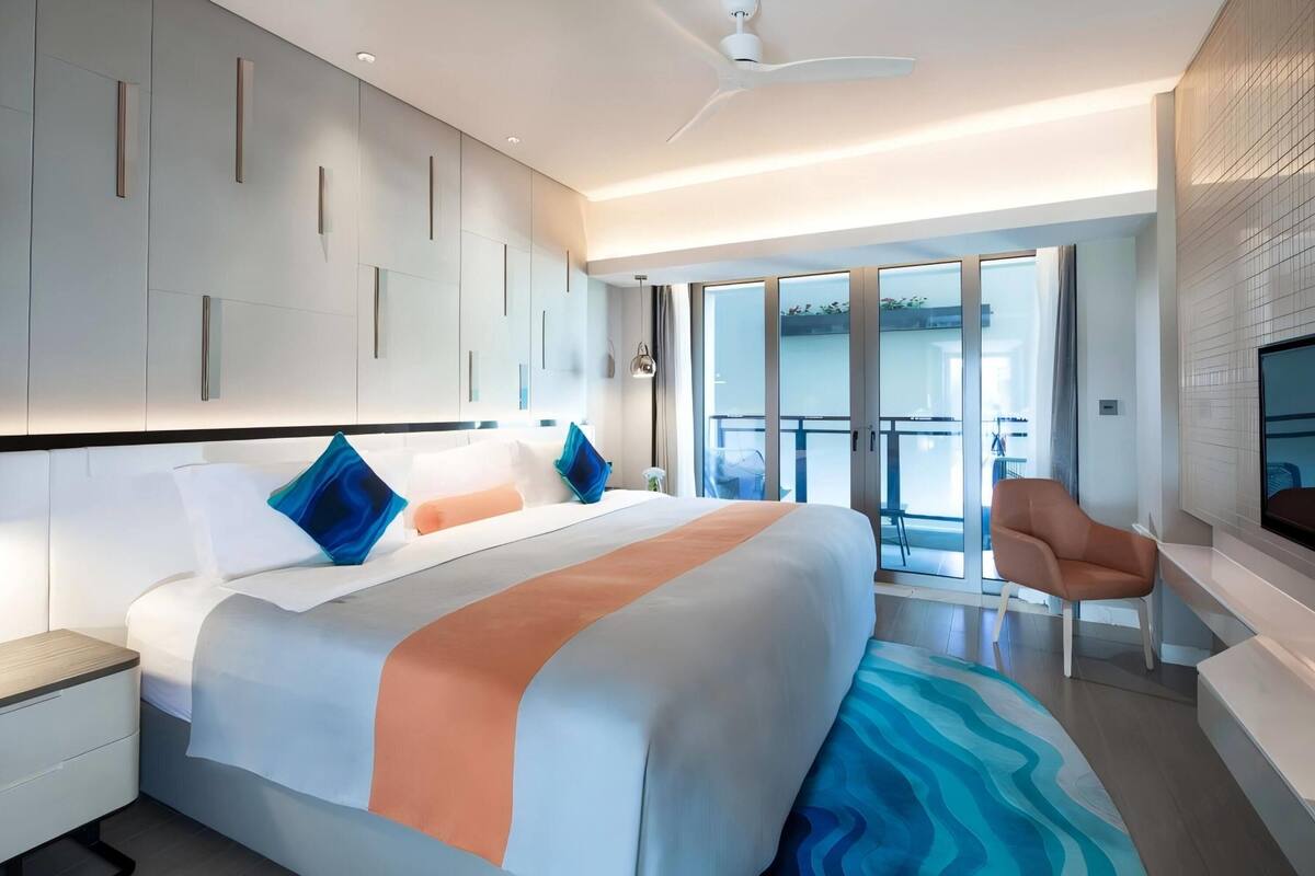 Een moderne hotelkamer met een groot bed, een flatscreen televisie, een balkon met uitzicht en een plafondventilator.