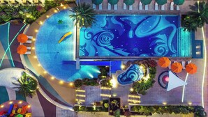 Vue aérienne d’un espace piscine d’hôtel, avec une fontaine centrale, des chaises longues disposées tout autour et des plantes décoratives.