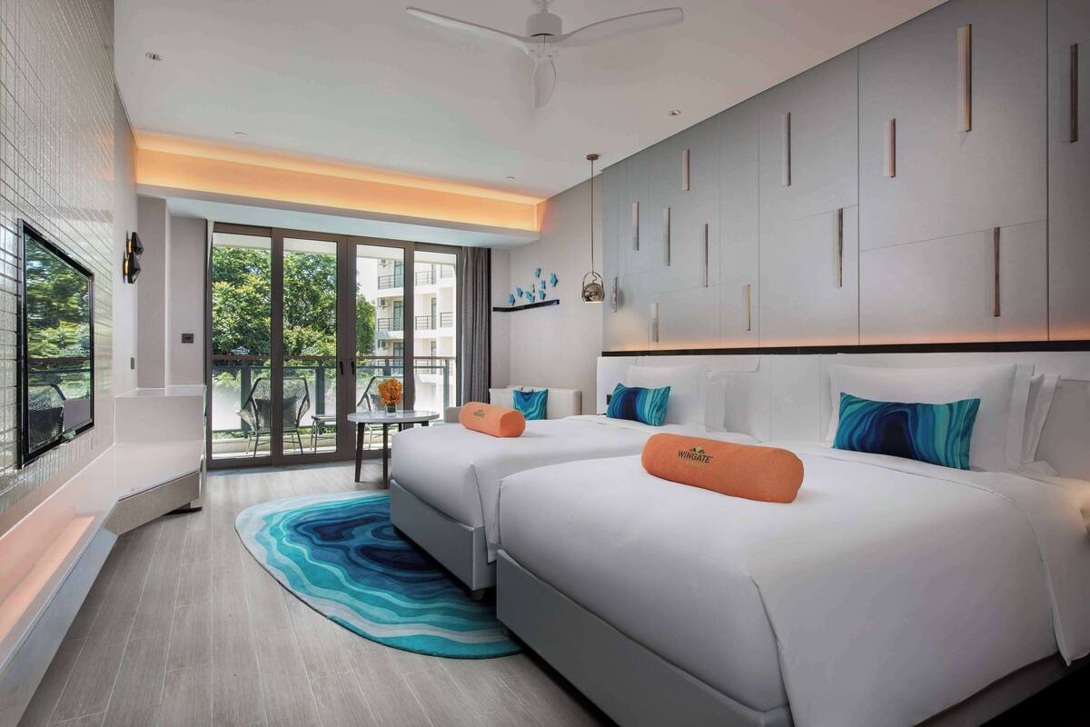 Hotelkamer met twee bedden, een groot raam, een plafondventilator en uitzicht op groen.