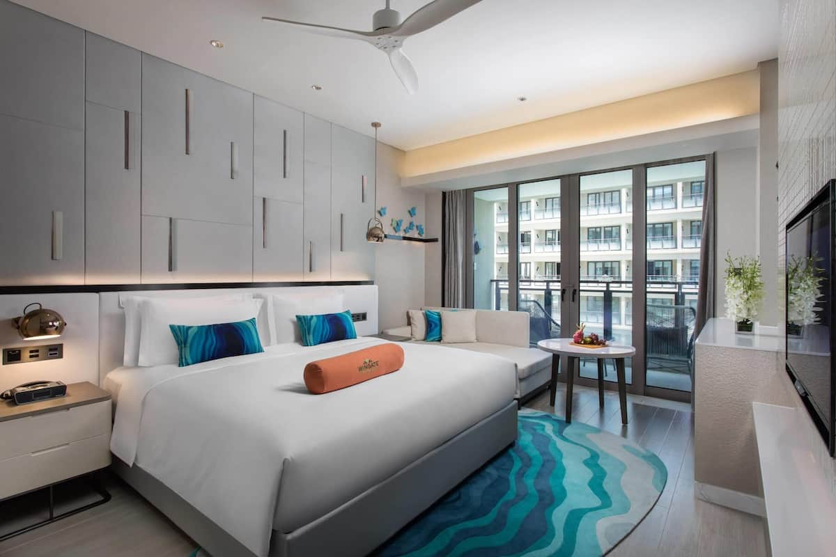 Een moderne hotelkamer met een groot bed, een klein tafeltje, een bank en een balkon met uitzicht op de stad.