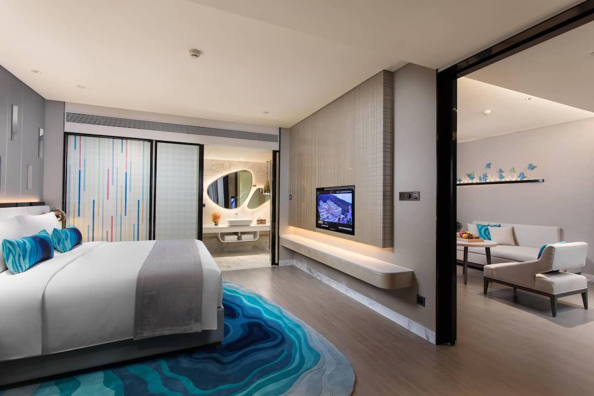 Een moderne hotelkamer met een groot bed, een televisie, een bank en een badkamer met een wastafel.