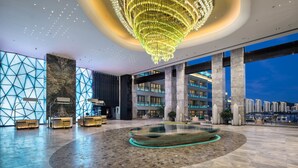 Un hall d’entrée spacieux, agrémenté d’un grand lustre, de coins salon et offrant une vue sur le panorama urbain.