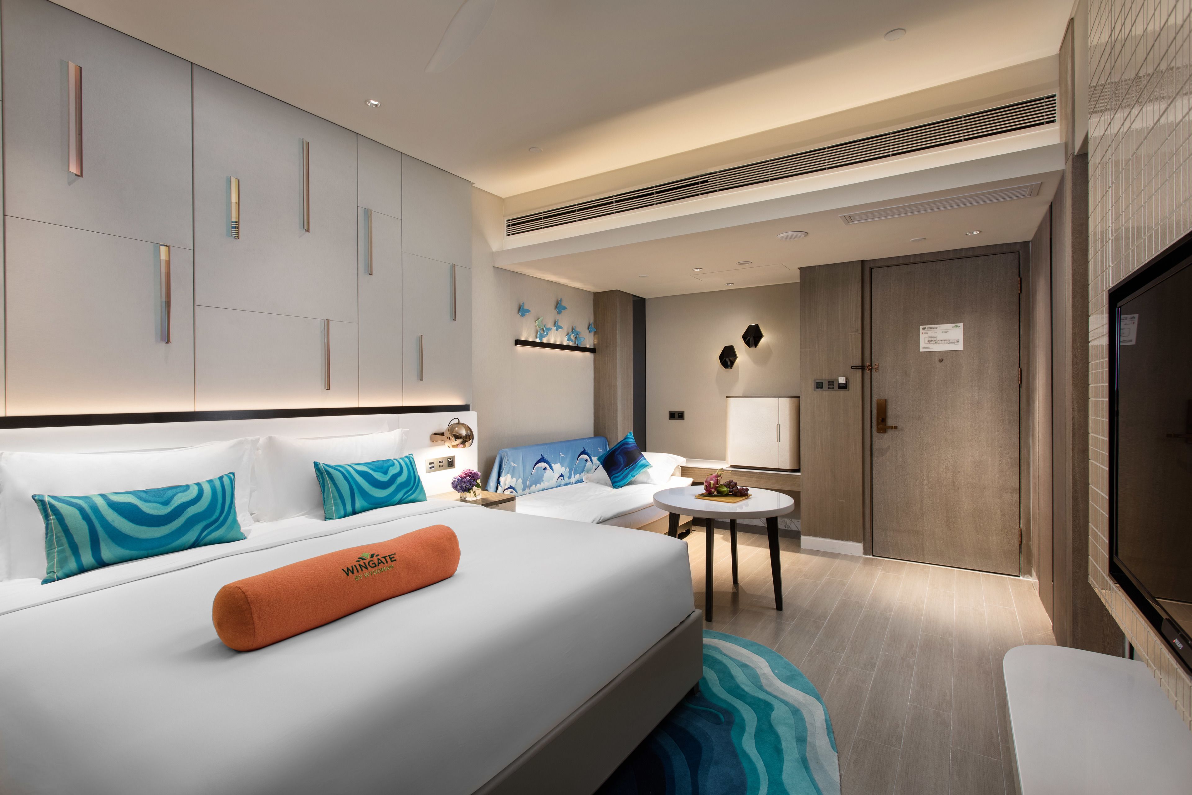 A modern hotel room with a large bed, a small seating area, and a TV.