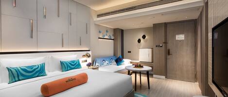 A modern hotel room with a large bed, a small seating area, and a TV.