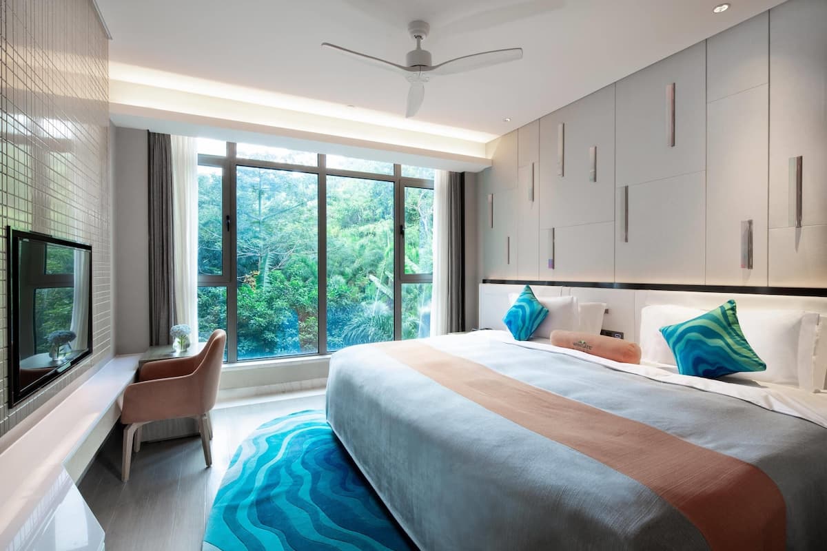 Een moderne hotelkamer met een groot bed, een bureau, een televisie en uitzicht op groen buiten het raam.