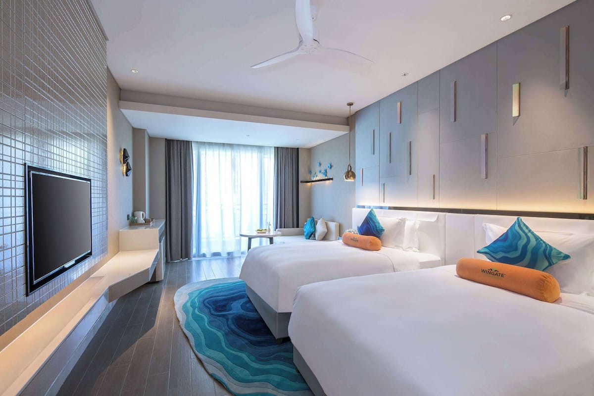 Hotelkamer met een flatscreen televisie, twee bedden, een plafondventilator, een groot raam en een modern design.