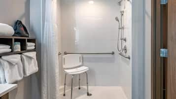 Un área de ducha moderna con pared de azulejos blancos, un cabezal de ducha, una ducha de mano, una barra de apoyo y una silla blanca.