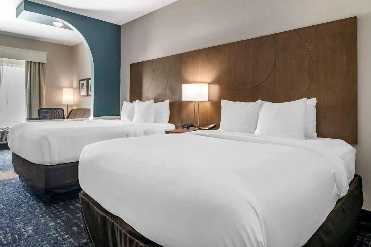A hotel room with two beds, a wooden headboard, a lamp, and a view of the hallway.