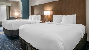 Habitación de hotel con dos camas, cabecero de madera, escritorio con lámpara y vista al pasillo.