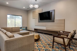 A modern living room with a sofa, chairs, a coffee table, a flat-screen TV, and a patterned carpet.