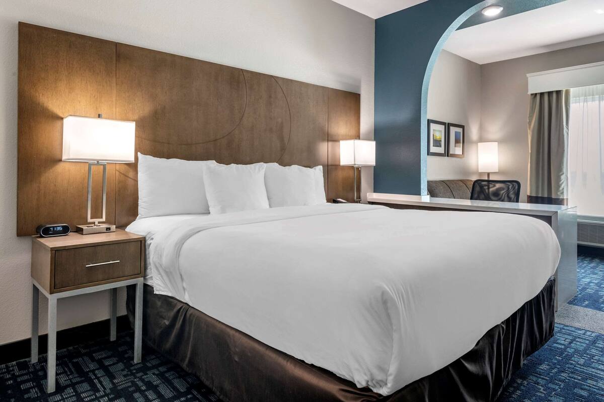 A hotel room with a large bed, two bedside tables with lamps, a nightstand, a mirror, and a view of the outside.