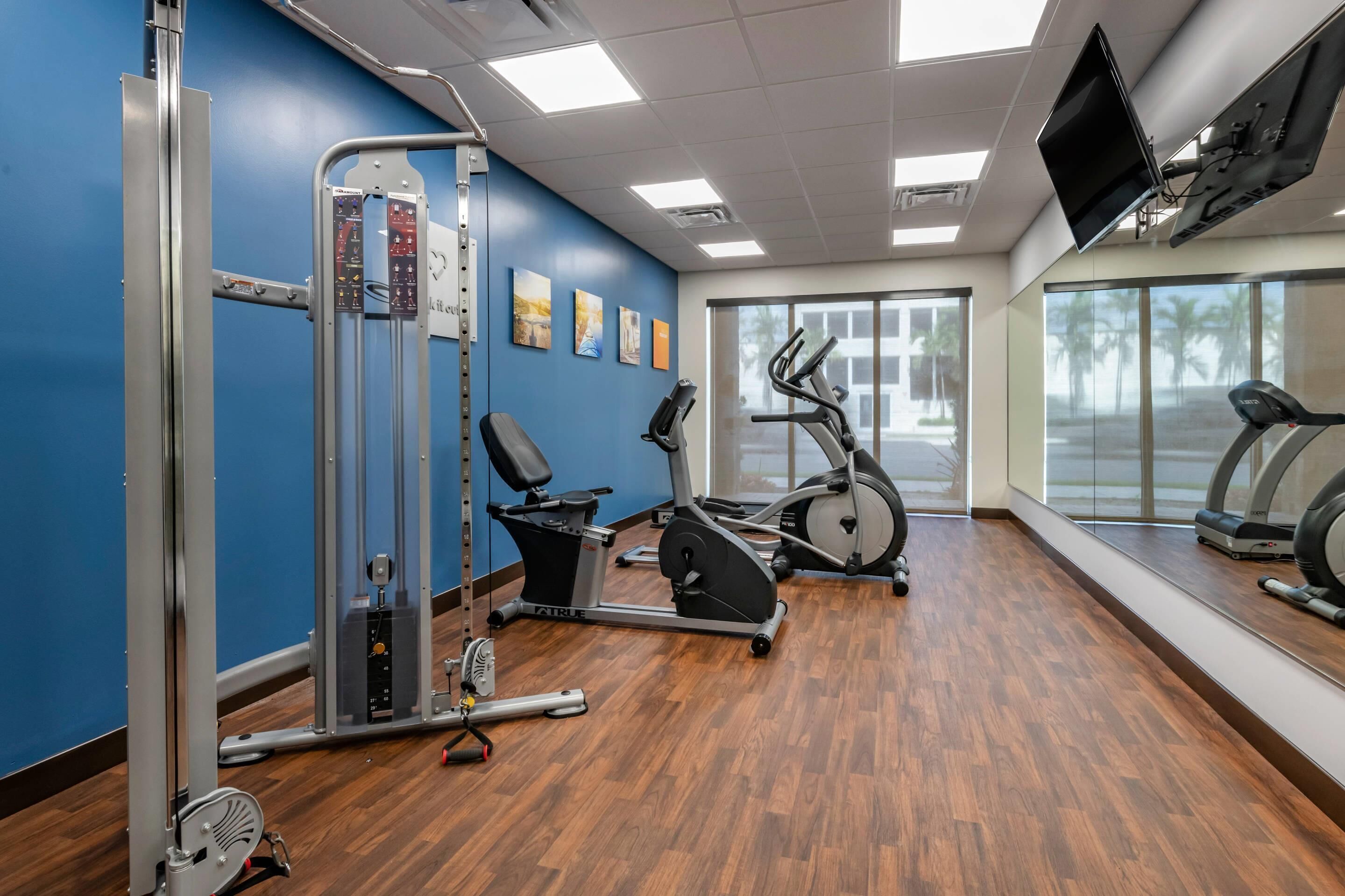 Una palestra con attrezzature per esercizi, una televisione e ampie finestre.