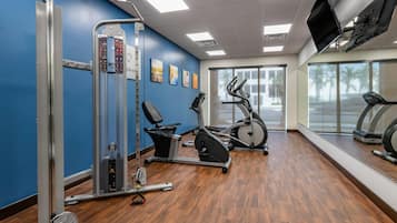 Una palestra con attrezzature per esercizi, una televisione e ampie finestre.