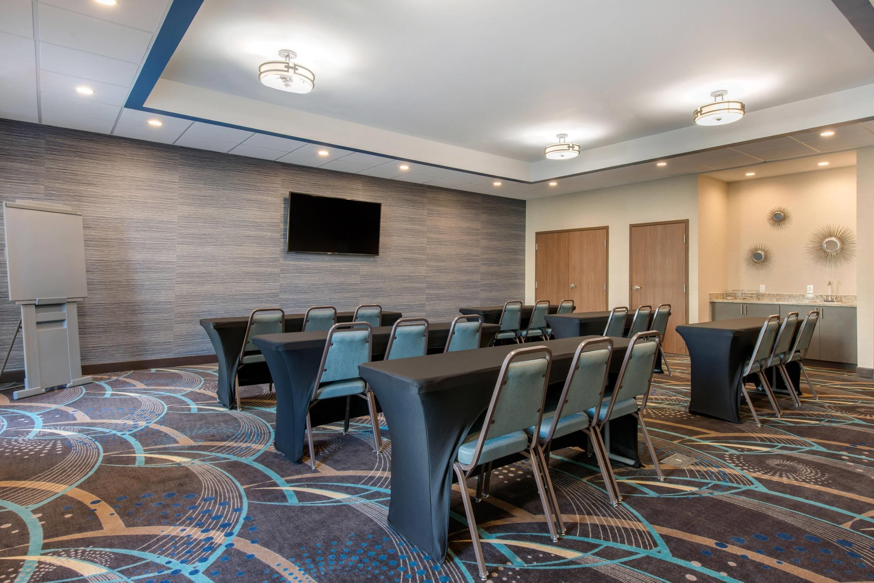 A conference room with a large table, chairs, a flat-screen TV, and a whiteboard.