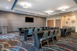 Un salón de conferencias con una gran mesa, sillas, una televisión de pantalla plana y una pizarra.
