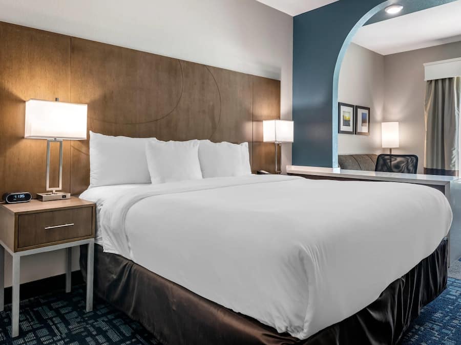 A hotel room with a large bed, two bedside tables, a nightstand, a mirror, and a view of the hallway.