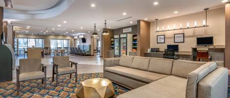 A hotel lobby with a seating area, a kitchenette, and a view of the dining area.