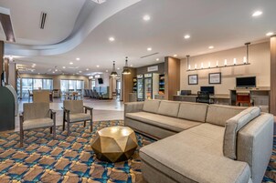 A hotel lobby with a seating area, a kitchenette, and a view of the dining area.