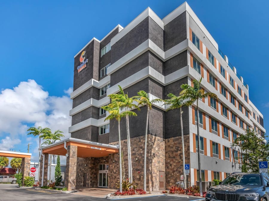 A multi-story hotel with a modern architectural design, featuring a prominent entrance with a covered area and palm trees.