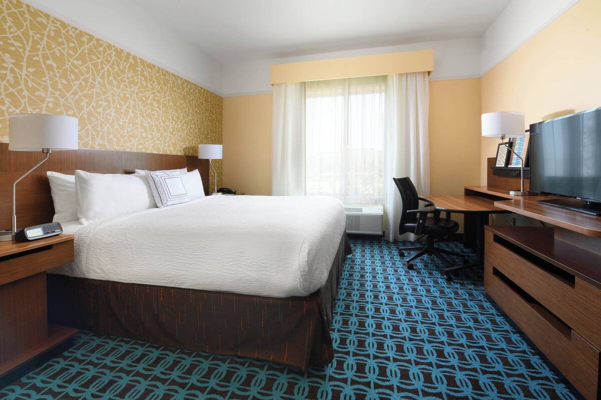 Een hotelkamer met een groot bed, een bureau met stoel, een televisie en een raam met gordijnen.