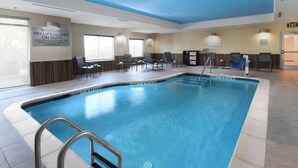 Una piscina interior con un cartel de advertencia para salvavidas, sillas de descanso y techo transparente.