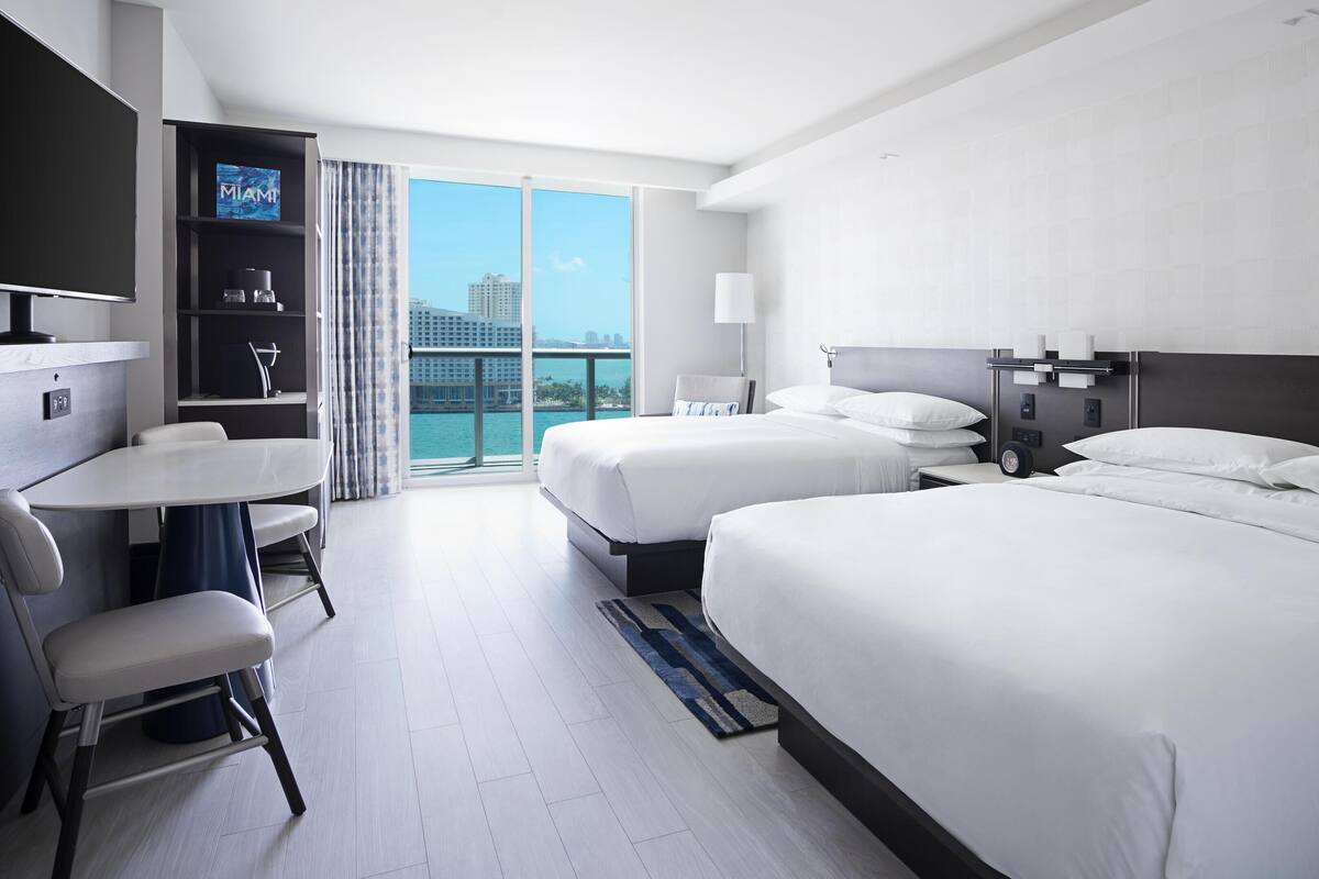 A hotel room with two beds, a desk, and a TV.
