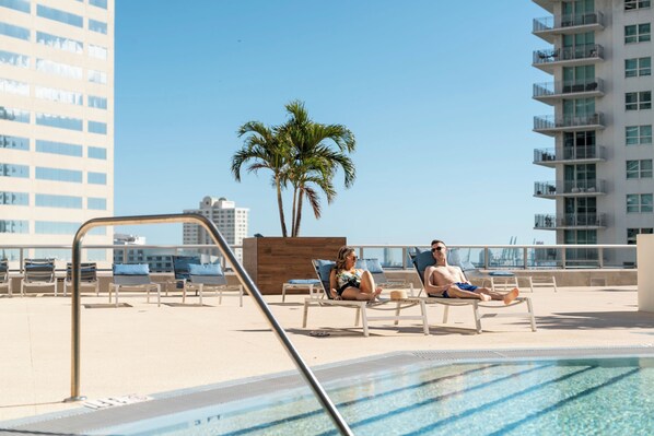 Una piscina al aire libre, sombrillas, sillones reclinables de piscina