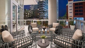 A balcony with wicker furniture, a central table with candles, and a view of tall buildings at night.