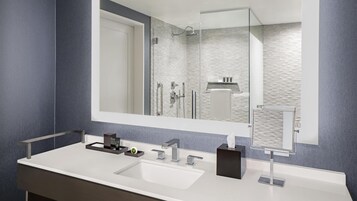 Un bagno moderno con uno specchio grande, un lavandino bianco e una cabina doccia in vetro.