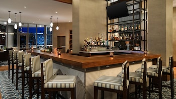 A conference room with round tables, blue chairs, and white tablecloths. Large windows offer a view of a body of water and high-rise buildings. at Hyatt Centric Brickell Miami