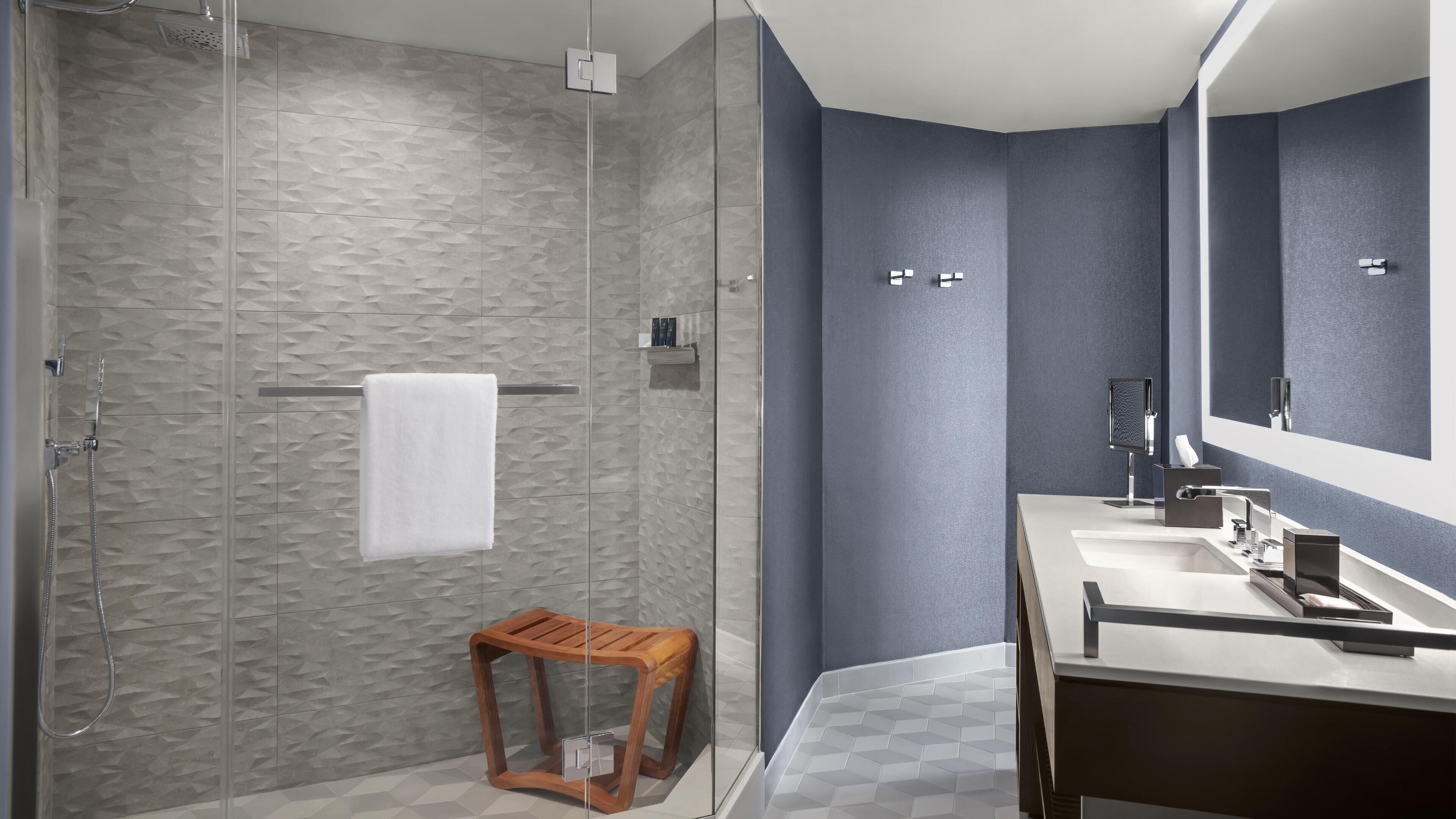 A modern bathroom with a walk-in shower, a wooden stool, a large mirror, and a vanity with a sink.