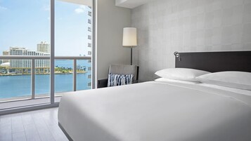 Camera d'albergo moderna con un letto grande, un comodino, una lampada e vista sullo skyline cittadino e sull'acqua.