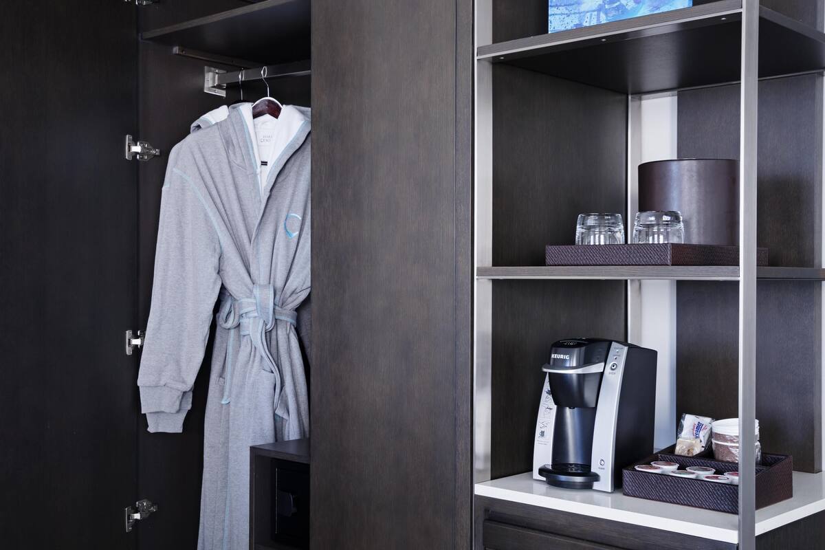 A hotel room with a robe hanging on a rack, a coffee maker, and a tray with cups and a box of tissues.