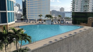A rooftop pool with lounge chairs and palm trees, surrounded by high-rise buildings.