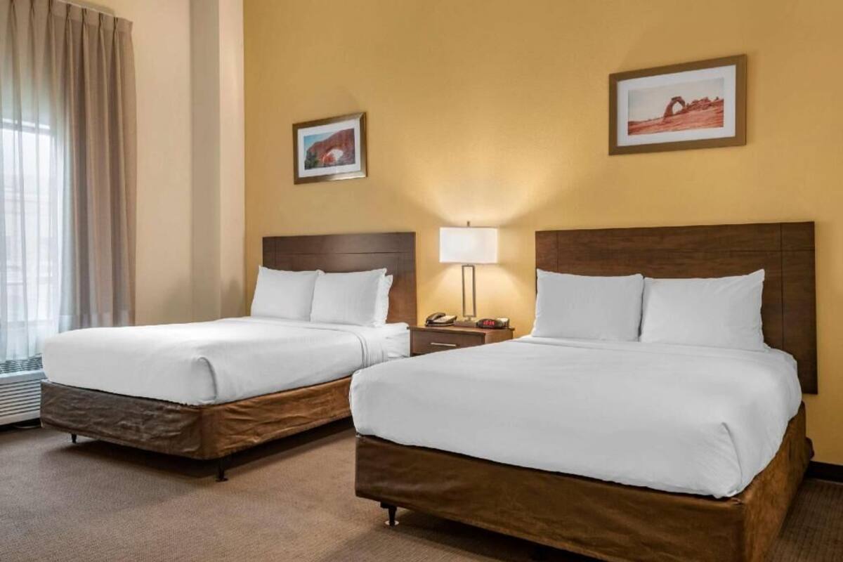 Habitación de hotel con dos camas, una mesita de noche con lámpara, y dos cuadros enmarcados en la pared.
