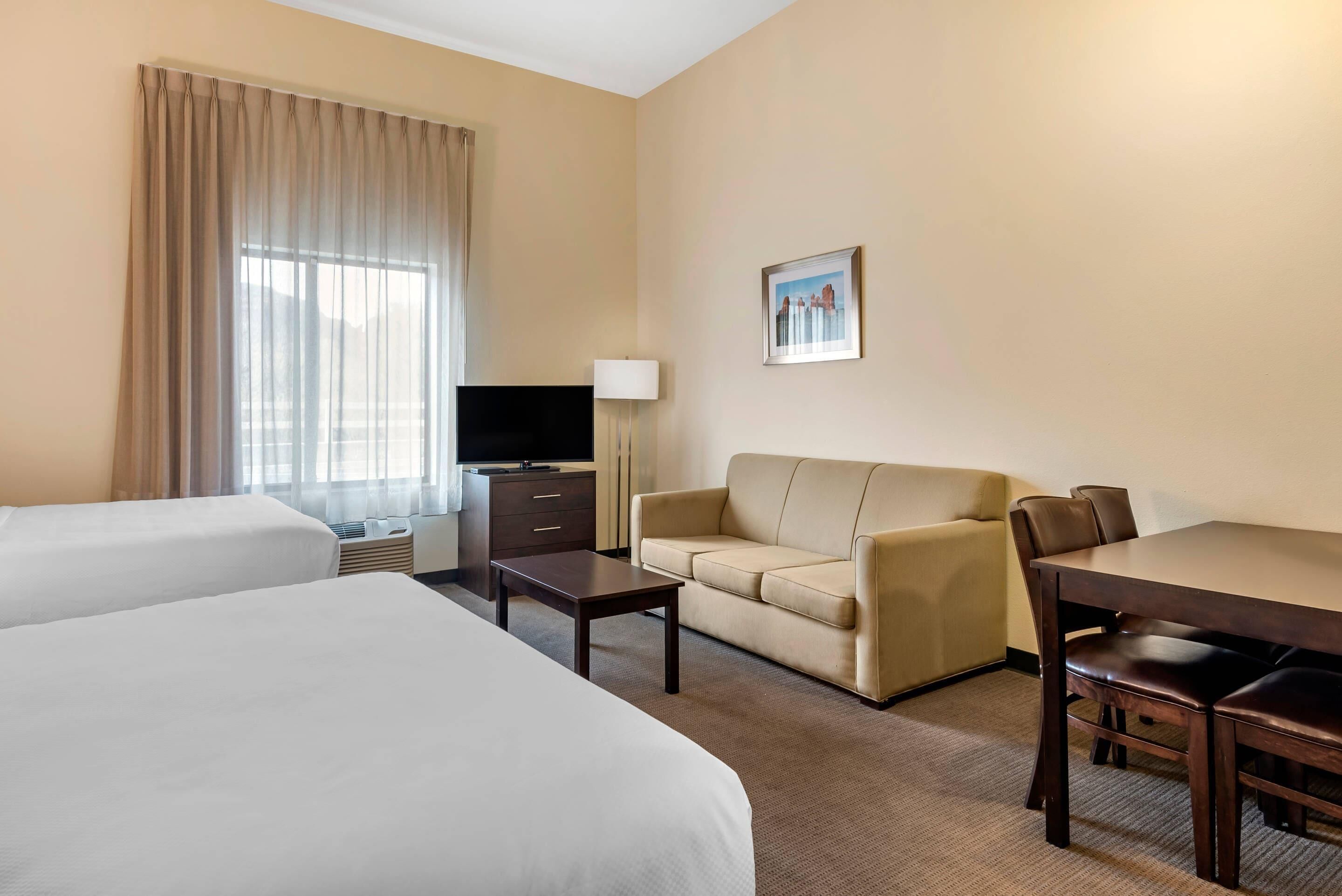 A hotel room with two beds, a sofa, a TV, a desk, and a lamp.
