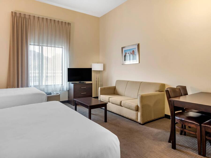 A hotel room with two beds, a sofa, a TV, a desk, and a lamp.