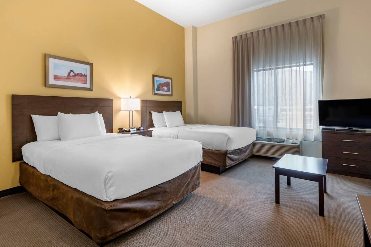 Habitación de hotel con dos camas, televisión, escritorio y ventana con cortinas.