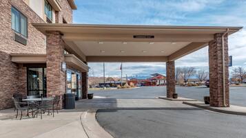 A hotel entrance with a covered parking area, outdoor seating, and a clear view of the surrounding landscape.